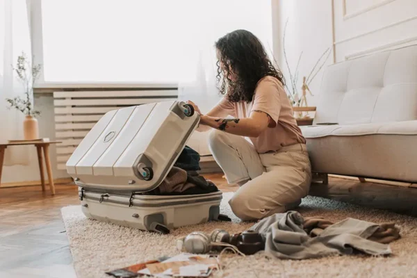 Traveler kneeling on a rug packing clothes into a white suitcase in preparation for a tour.