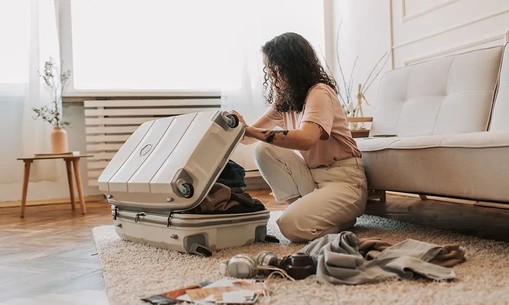 Traveler kneeling on a rug packing clothes into a white suitcase in preparation for a tour.