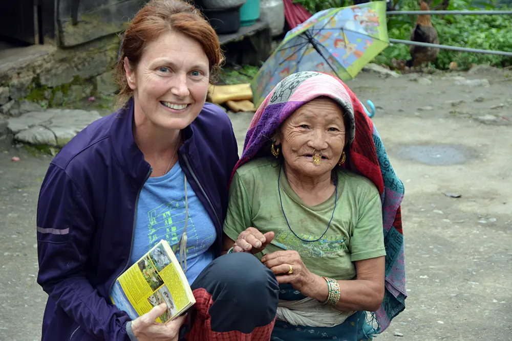 Smiling foreign tourist holding a guidebook posing with an elderly local woman in Sikkim.