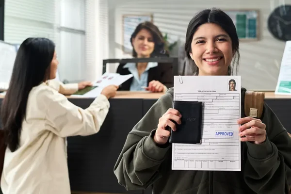 Smiling traveler holding an approved visa application form and passport at a processing center.