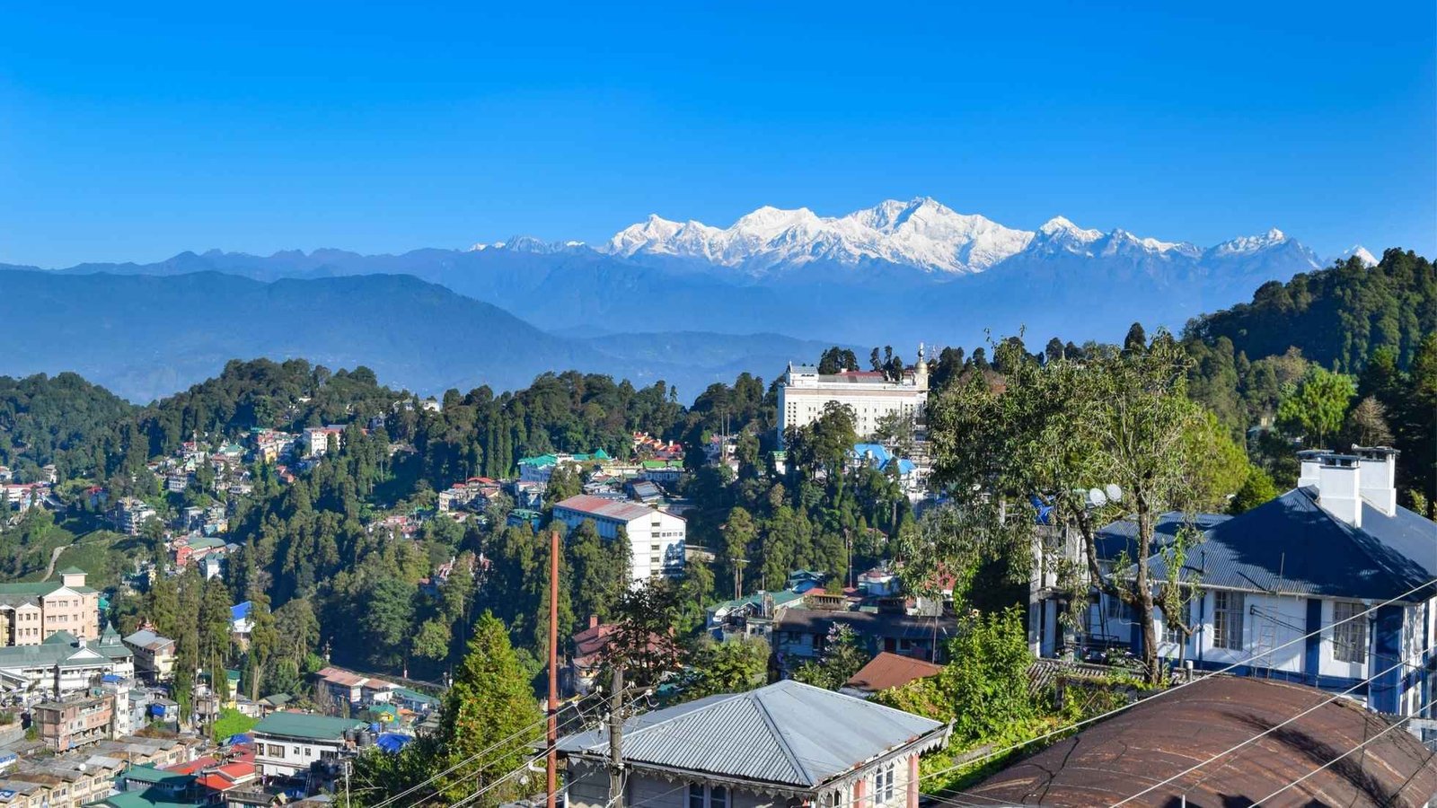 Scenic Darjeeling town nestled in the Himalayas, offering a clear view of the majestic Kanchenjunga peaks under a blue sky