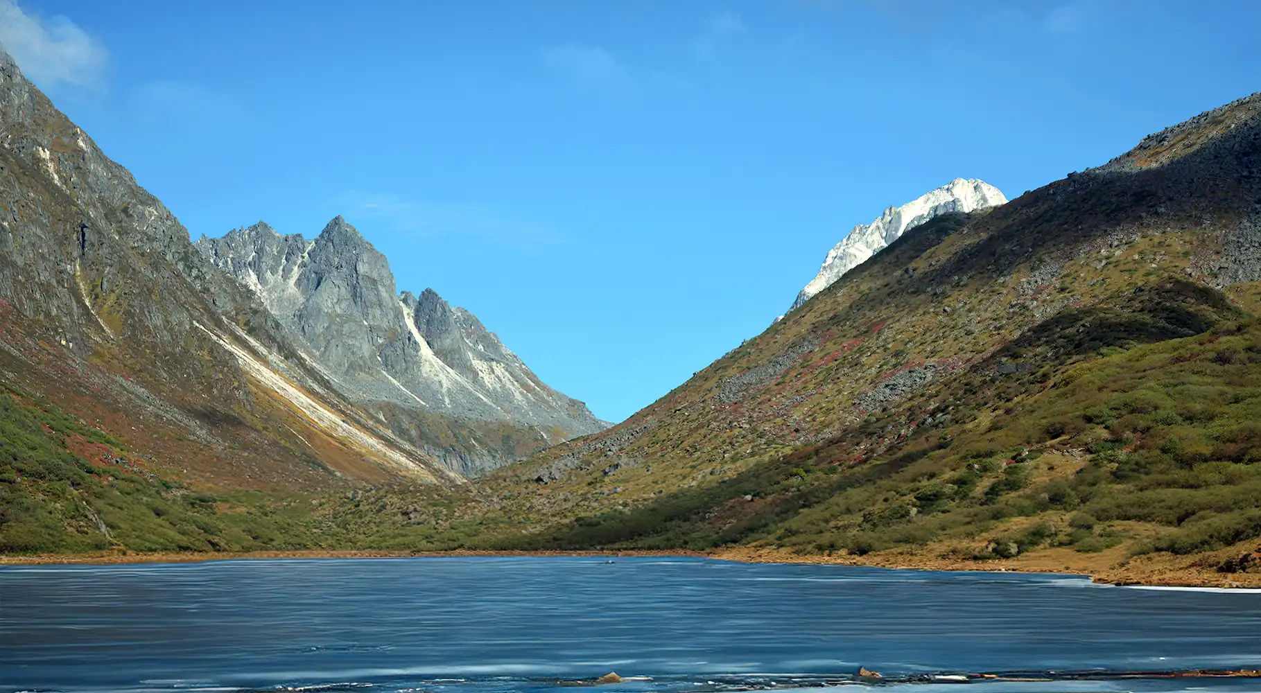 Pristine alpine lake surrounded by snow-capped Himalayan peaks during Uttarey Singalila Goechala trek in Sikkim with clear blue sky and autumn mountain slopes