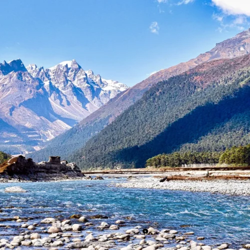 A clear blue river flowing through the scenic Yumthang Valley in North Sikkim, backed by snow-capped mountains.