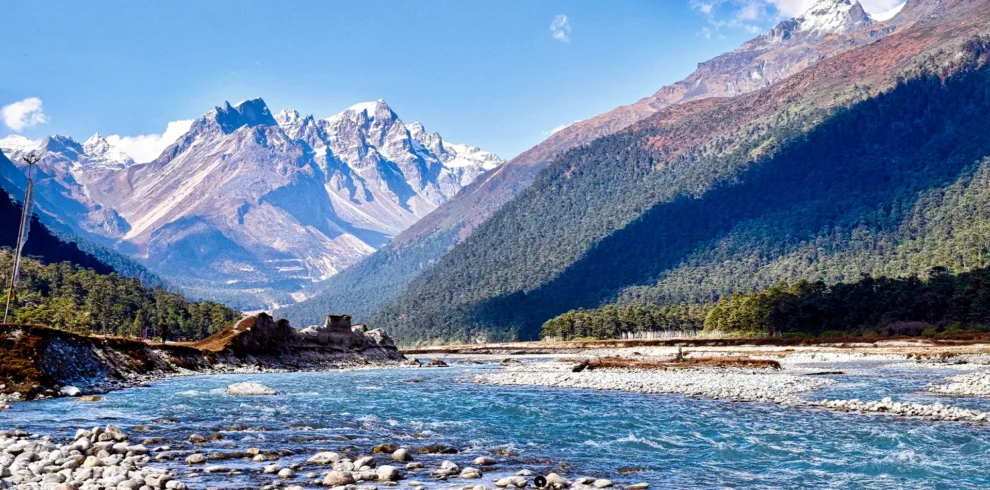 A clear blue river flowing through the scenic Yumthang Valley in North Sikkim, backed by snow-capped mountains.