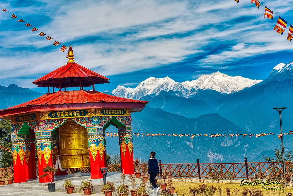 Epic view of a vibrant golden prayer wheel in Sikkim, framed by flying flags and the towering Mt. Kanchenjunga.